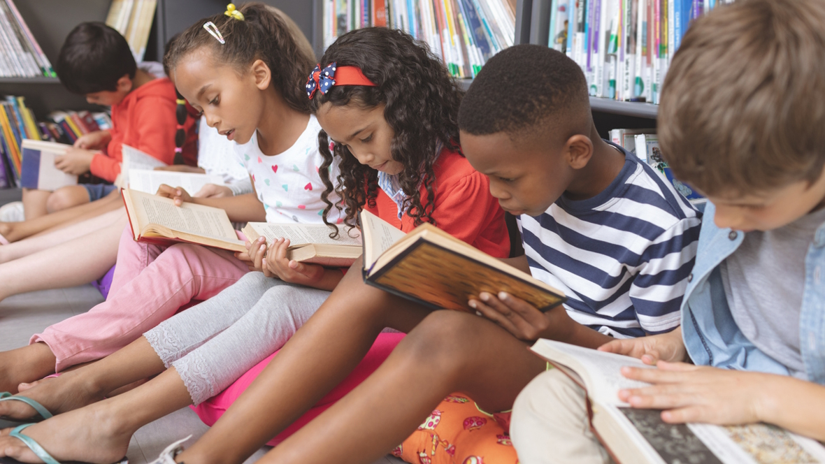group of kids reading books sitting on the floor in a library