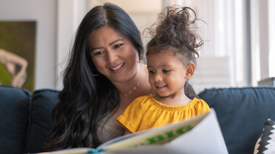 Mom and daughter sitting on a couch reading a book together