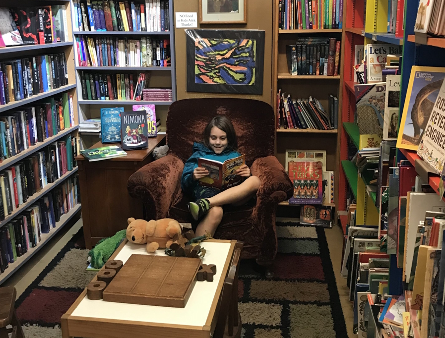 A boy in a kid-sized chair surrounded by book shelves at Couth Buzzard Books