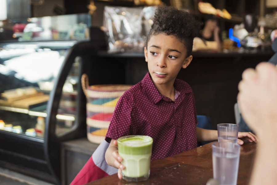 A young boy sitting in a coffee shop with a green drink