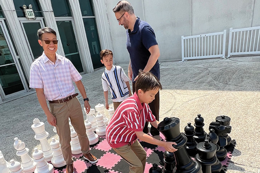 Moy and Varona playing a game of giant chess with their sons