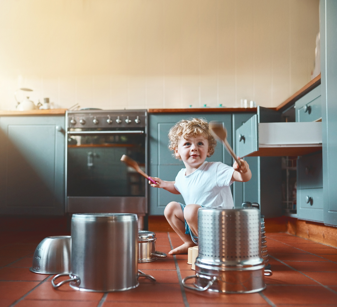 Portrait of an adorable little boy playing with pots in the kitchen