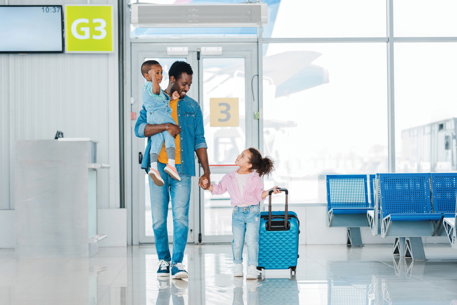 Father carrying baby and holding hand of a young girl pulling a suitcase in an airport