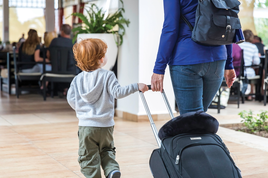 Young child holding on to a rolling suitcase with adult woman and walking 