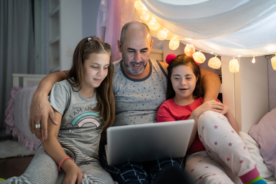 Dad watching tv on a computer with two daughters