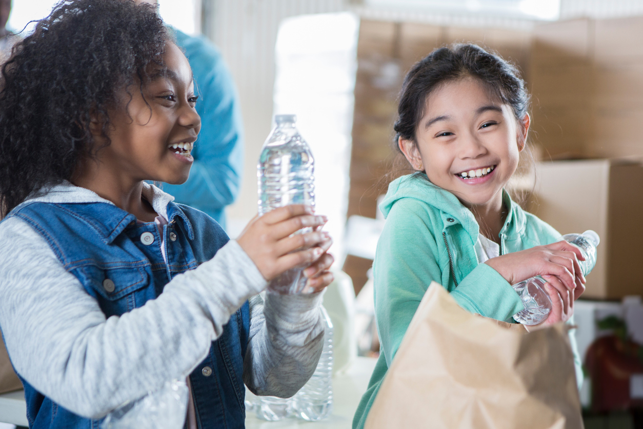 two kids filling paper bags with water bottles and canned goods