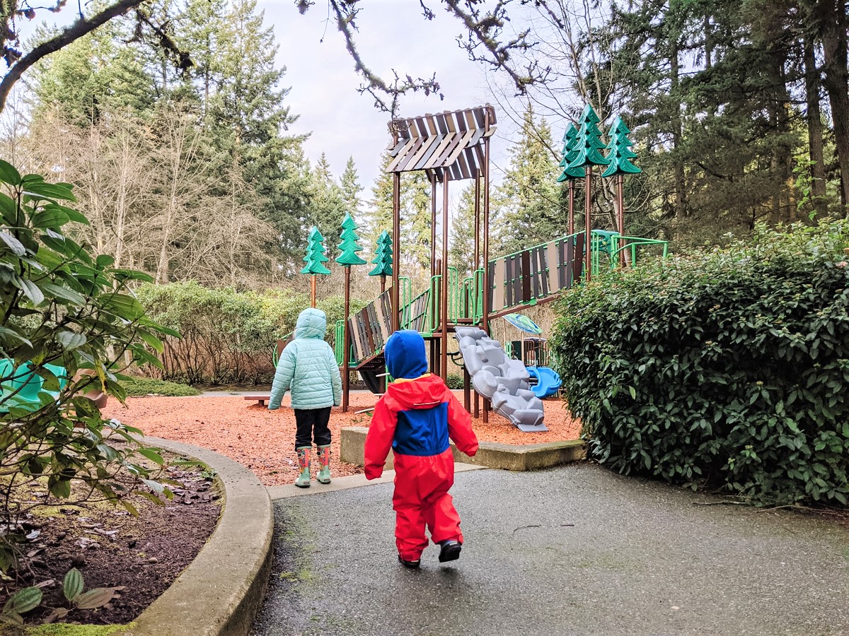 Young kids dressed for rainy weather approaching a new playground at Heron Park in Mill Creek, a small city near Seattle Washington