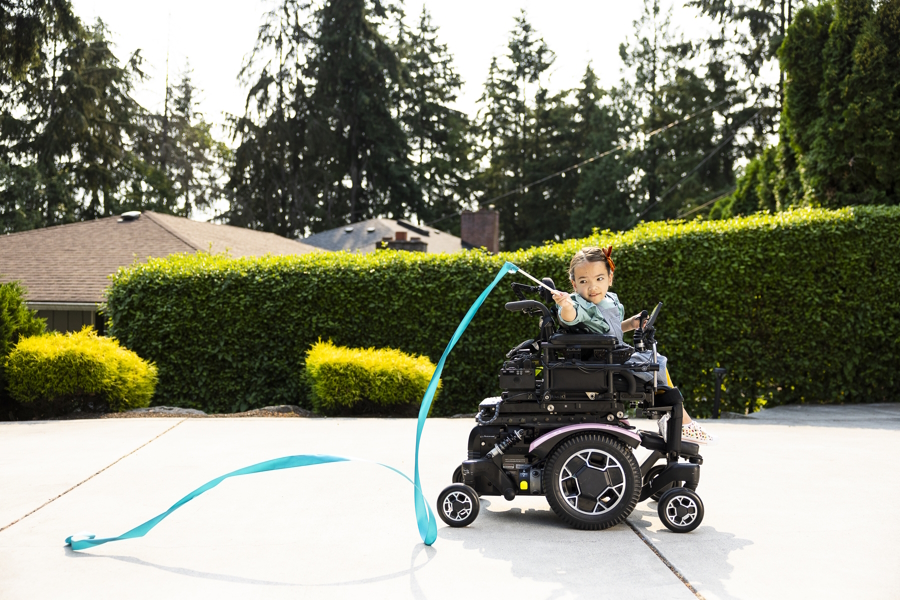 Hailee in her wheelchair playing with a long blue ribbon on a stick