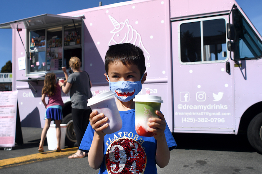 little boy with a shark mask holding two dreamy drinks with the dreamy drinks pink truck in the background