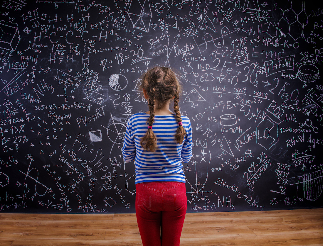 child standing looking at a blackboard covered with math