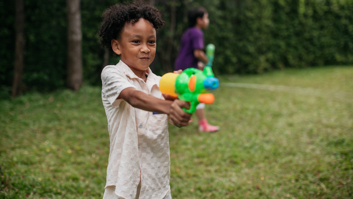 boy aiming a water squirter at a target outside in the summer