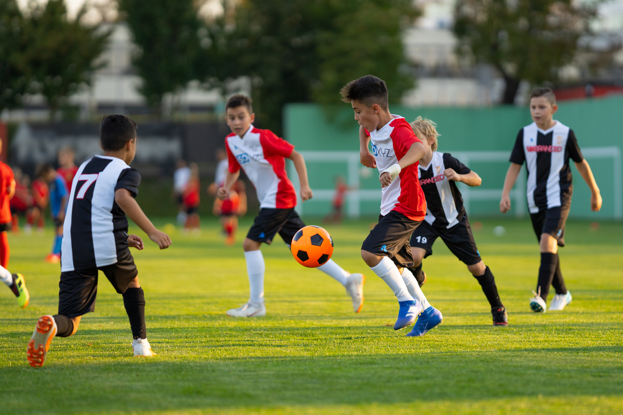 Kids of about middle school age, young teens, play in a soccer match while parents and families look on top tips for being a good sports parent