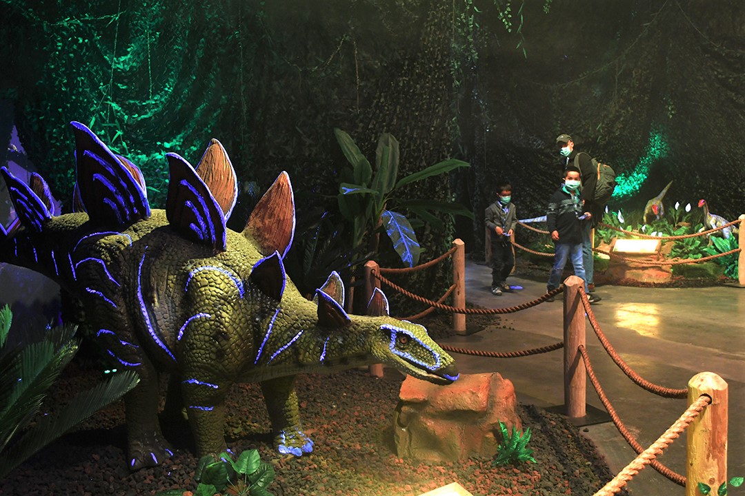 Kids wearing face masks walk past a stegosaurus model at Dinos Alive a new immersive dinosaur exhibit in Seattle's SODO neigbhorhood