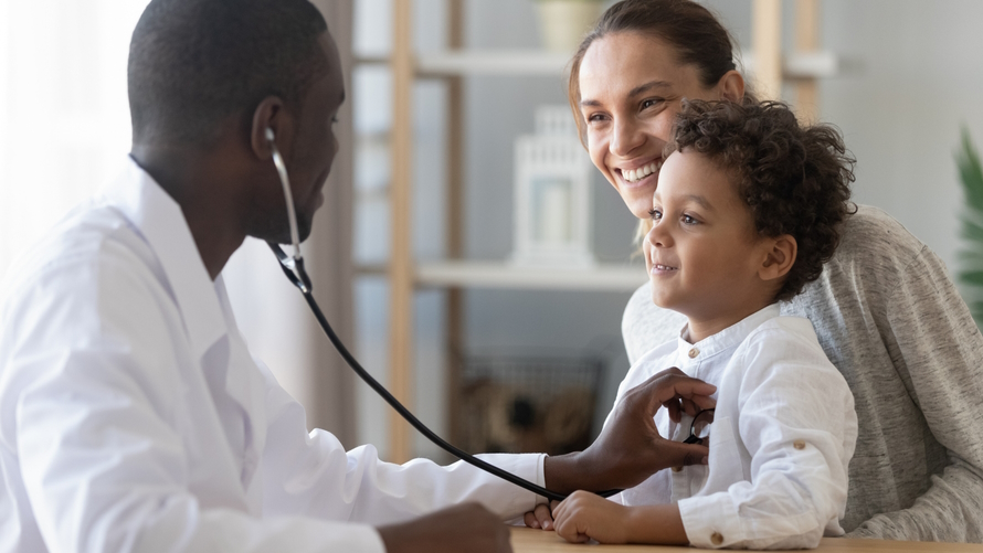 Doctor examining a young boy who is smiling and sitting on his mother's lap