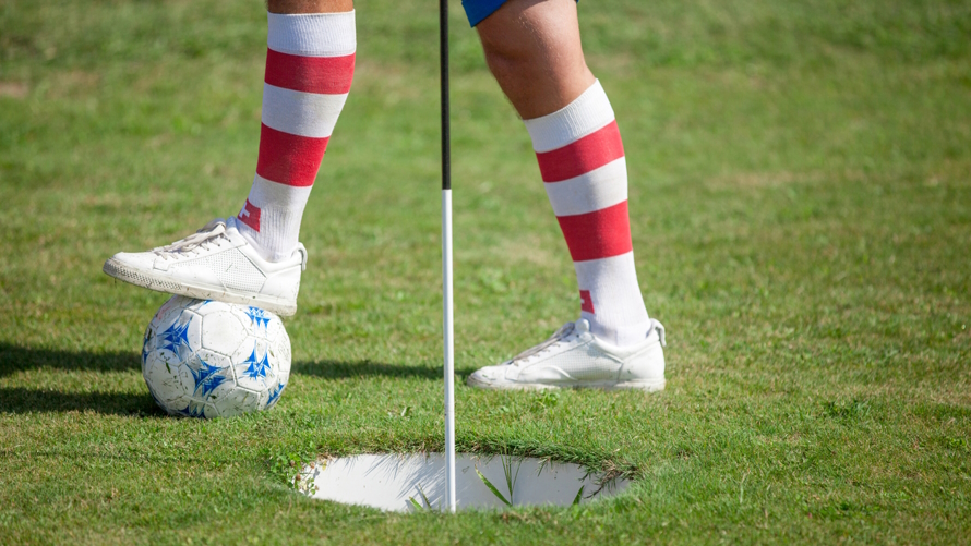 A foot and leg with a red and white striped sock playing footgolf