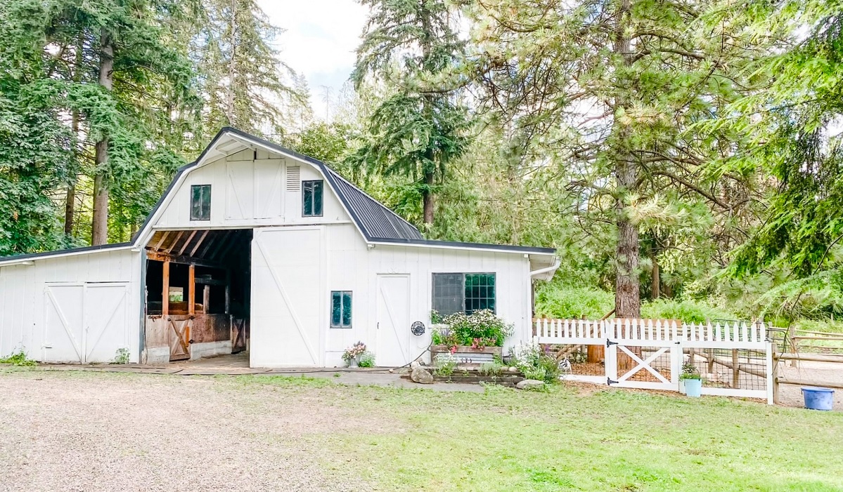 The white barn at Pivot Farm with trees in the background and grass in the foreground among sweet family farms for Seattle families to visit