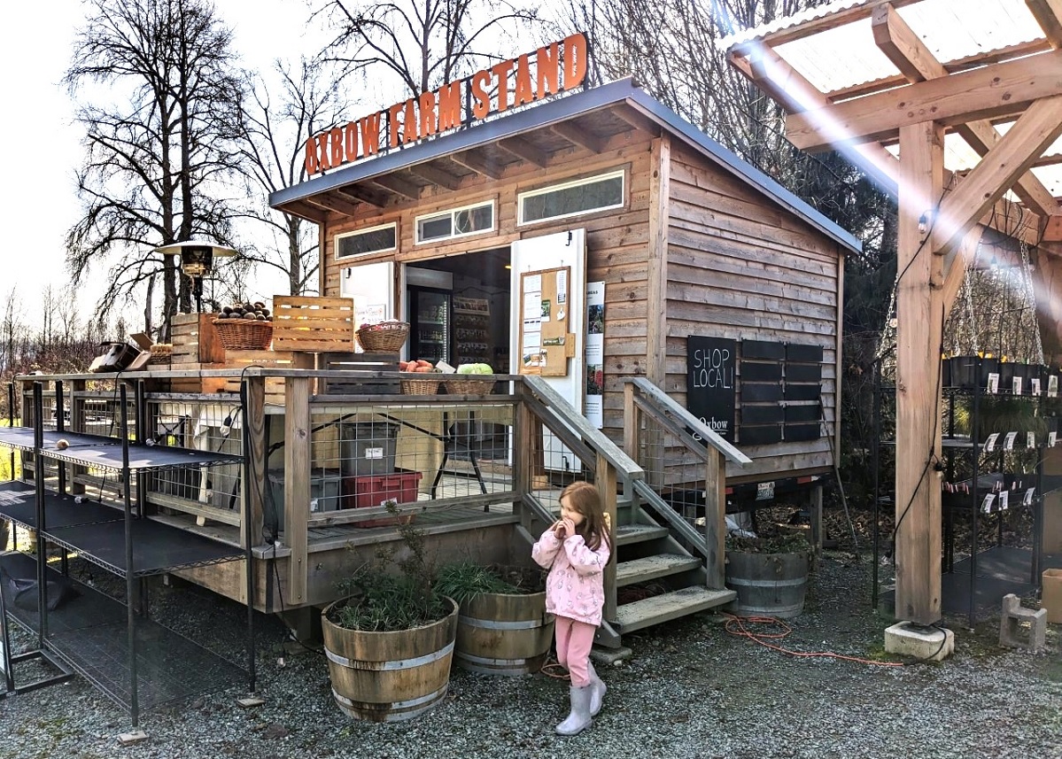 A young girl stands next to the farm stand selling fresh produce at Oxbow Farm near Seattle