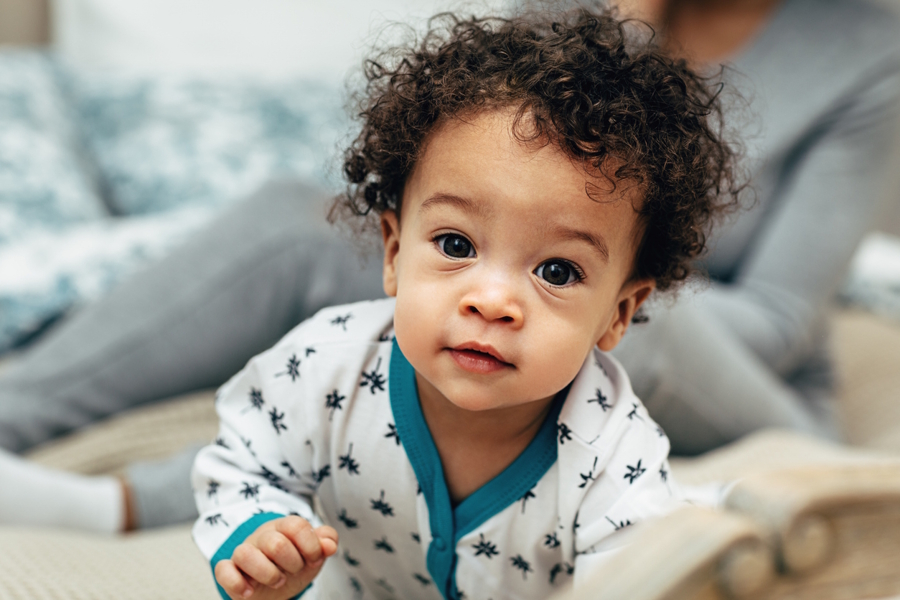 baby with curly hair looking at the camera and starting to smile