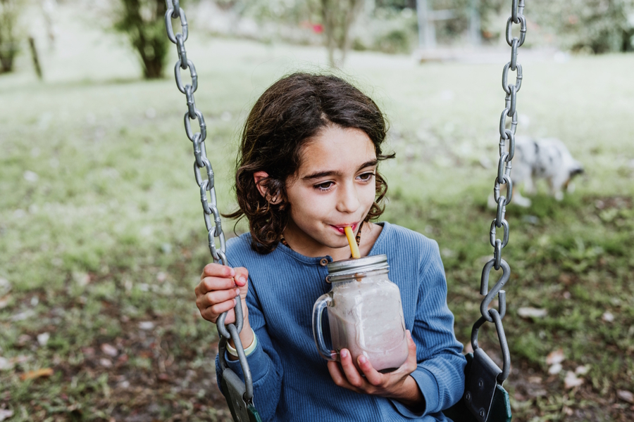 Girl sitting on a swing drinking a smoothie out of a glass jar with a straw