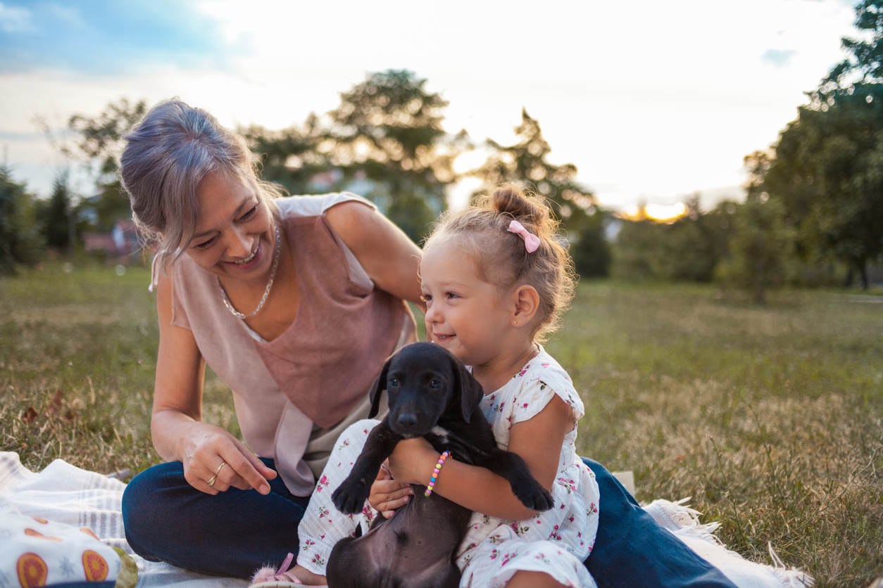 mother and daughter on a picnic blanket outside with a cute black puppy