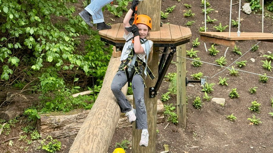 young girl on ropes course wearing a safety harness
