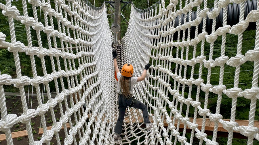young girl crossing a cargo net bridge on the ropes course at Bellevue Adventures Aerial Park