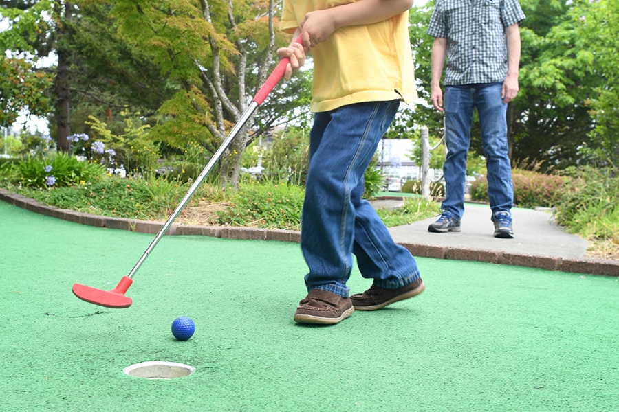 Outdoor and indoor mini golf two kids hitting a blue ball with a red putter