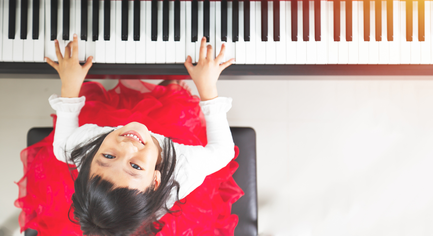 top-down photo of a girl in a red dress playing the piano while looking up at the camera