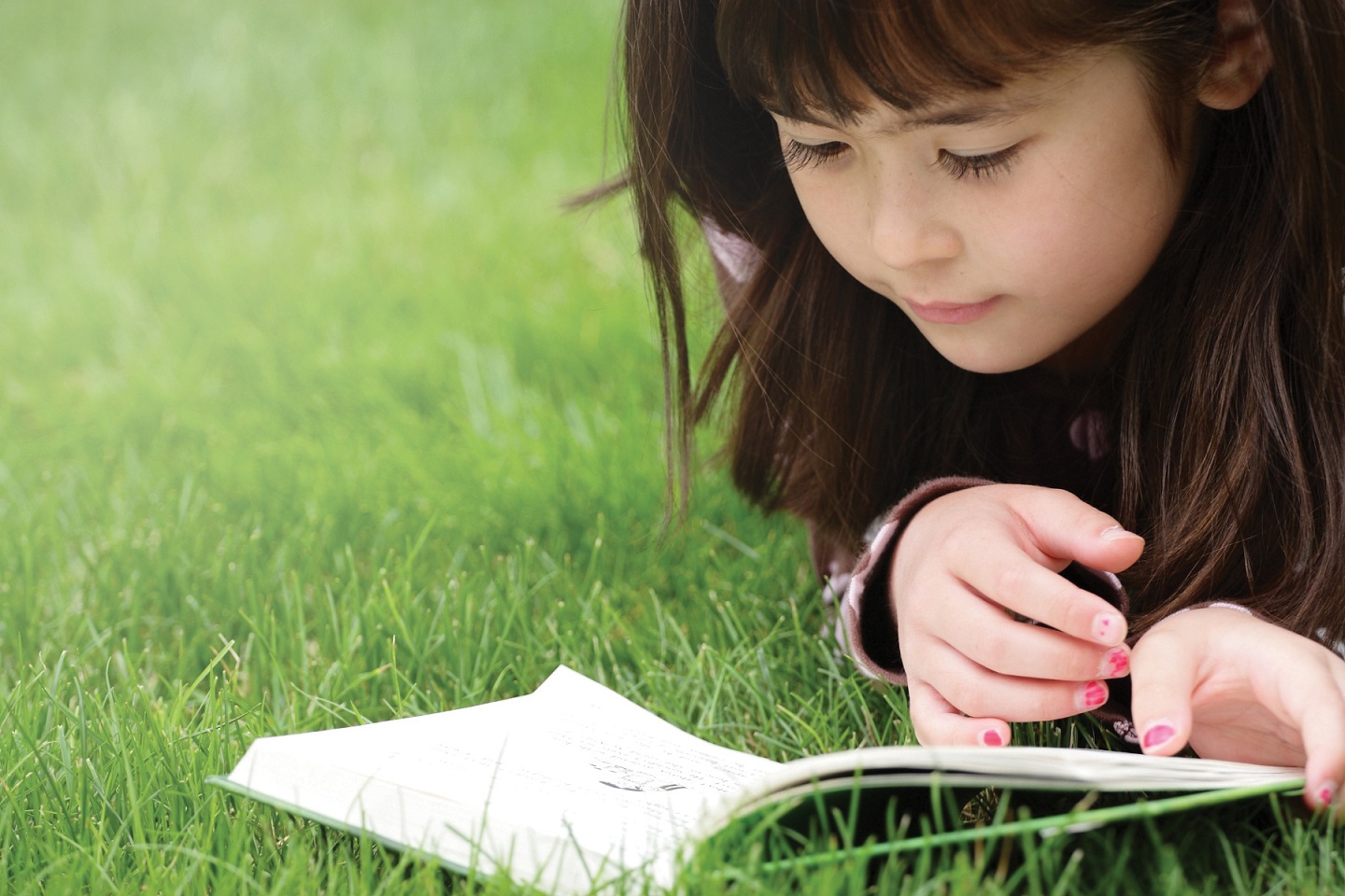 Young girl lying in the grass reading a book