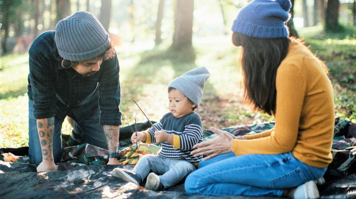 couple sitting with a baby on a blanket in the woods