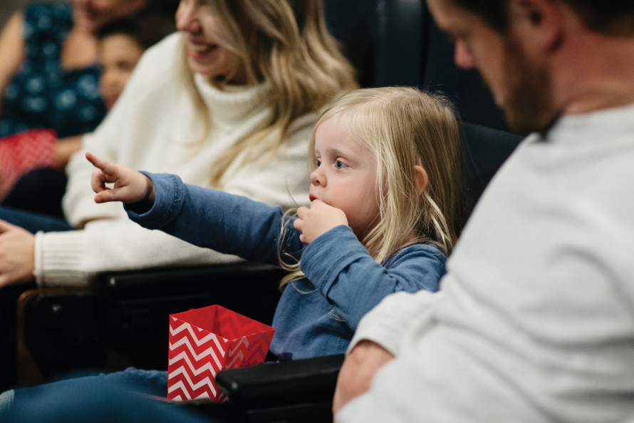 Young girl pointing and eating popcorn in a movie theater