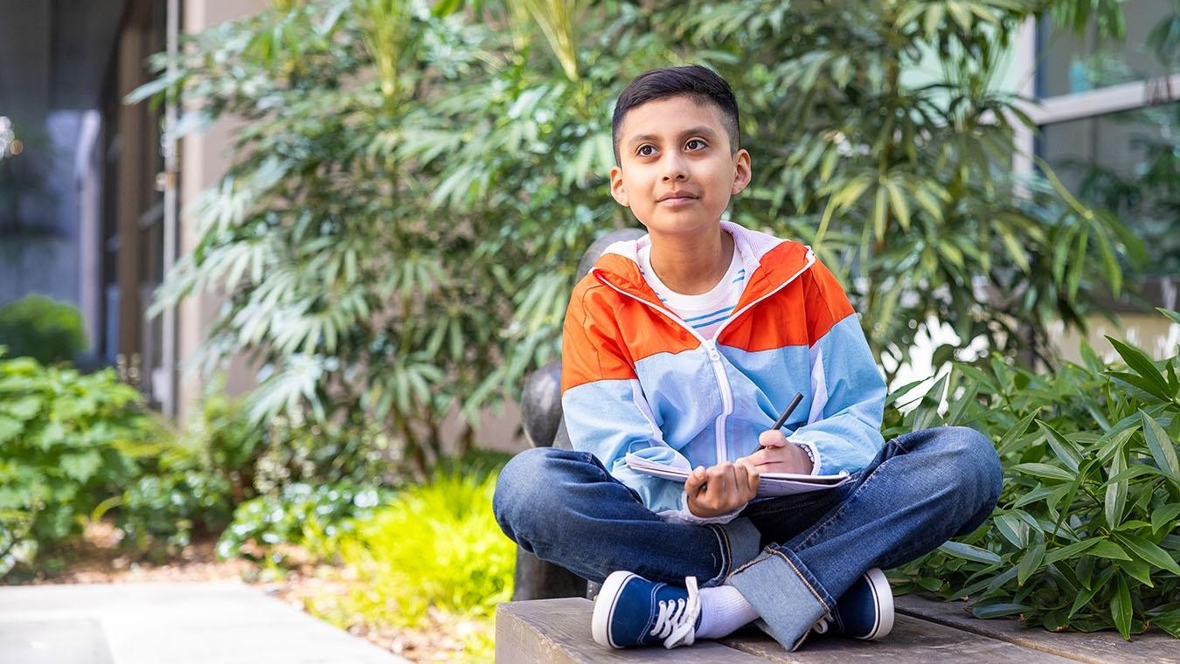 Ino sitting outside on a bench with a notebook and pencil in hand