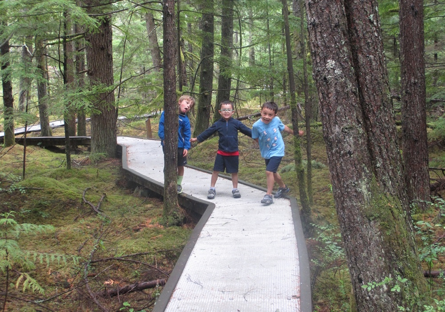 Three young boys on a boardwalk stroll through the woods