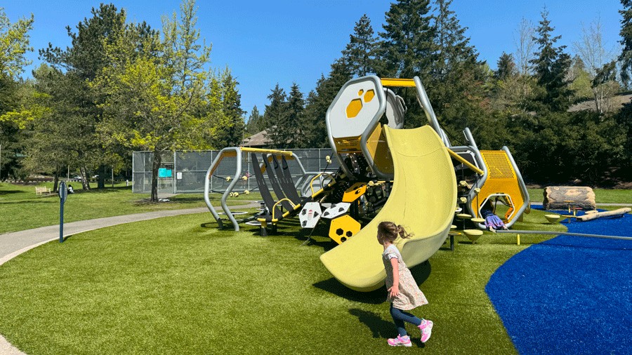 young girl running at Hidden Valley Park playground with a yellow slide and bee-themed structures