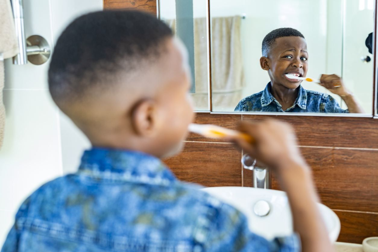 little boy brushing his teeth in front of the mirror