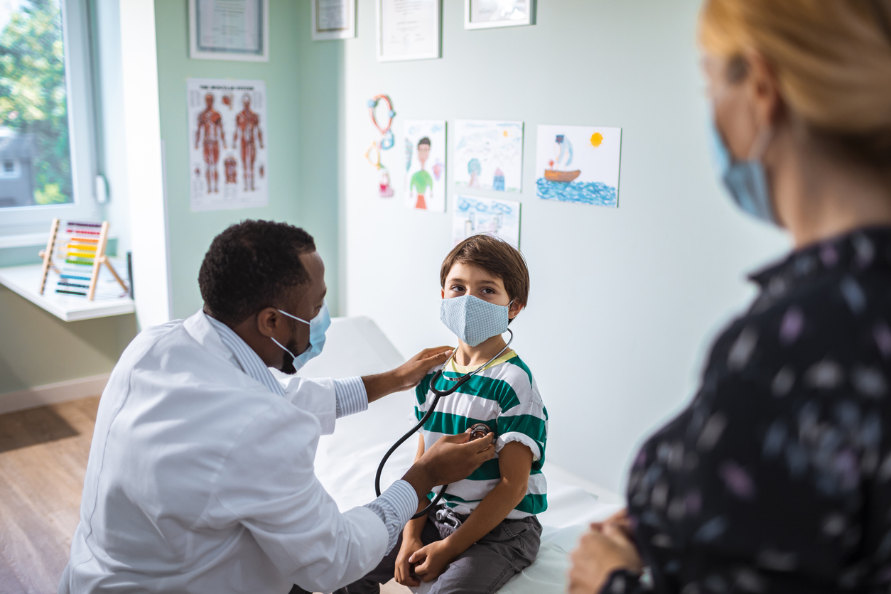 doctor listening to a child's heart with a stethoscope as the child's mother watches