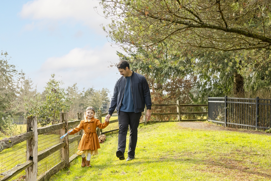 little girl and her dad walking next to a fence in the grass