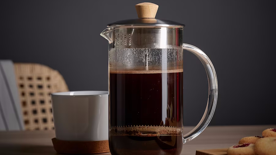 French press with coffee in front of a coffee cup