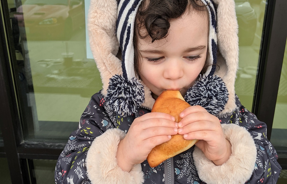 Young girl in warm jacket taking a bit of an East African coconut doughnut called mahamri Spice Bridge Food Hall Seattle Tukwila
