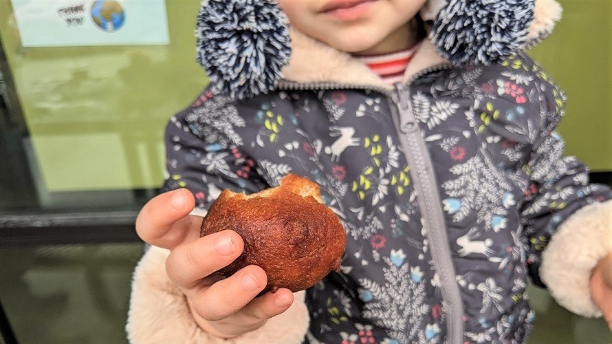 Close up of pastry being held by a young girl in a lavendar jacket whose mouth can just be seen spice bridge food hall seattle for families