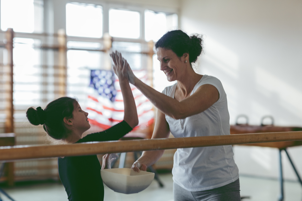 Cute little girl practicing gymnastics and giving her coach a high-five
