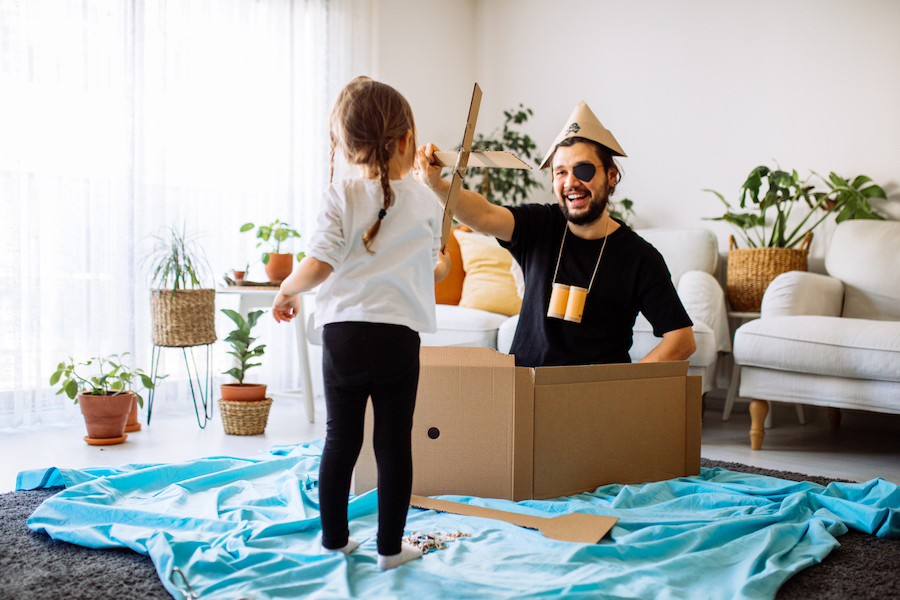 child plays in a box boat at home with dad