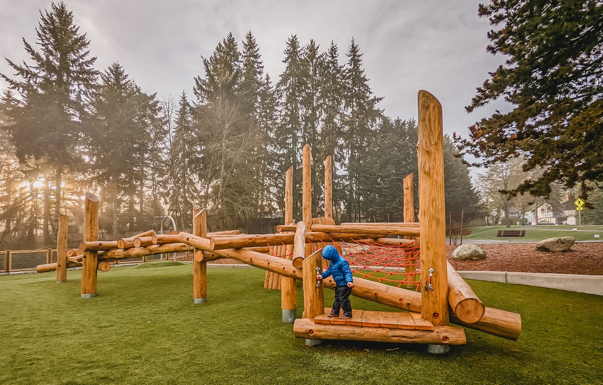 A small boy plays on wooden log play structures at new playground at Westside Park in Redmond, Washington, near Seattle