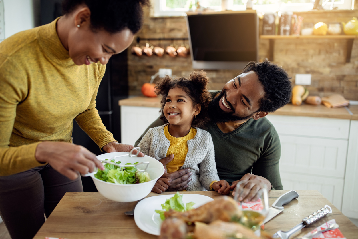 family of four in the kitchen with the mother serving a salad