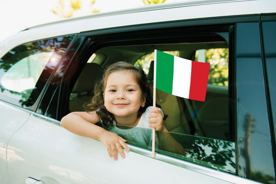 little girl looking out a car window smiling holding an Italian flag