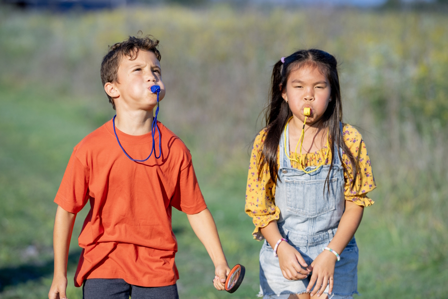 two kids blowing whistles outside