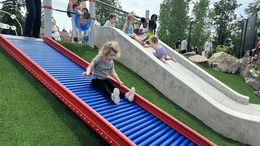 Young girl slides down a roller slide at a new inclusive playground near Seattle