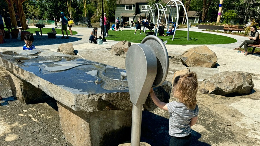 Young girl playing at the Pathways Park water table, with carved channels for water play