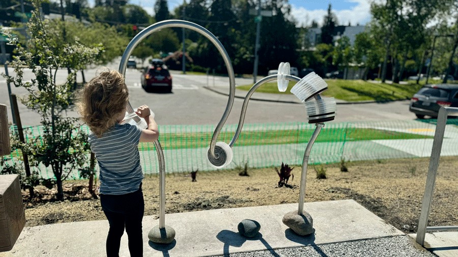 Young girl slides discs on an art sculpture at inclusive Pathways Park playground that recognizes donors and contributors