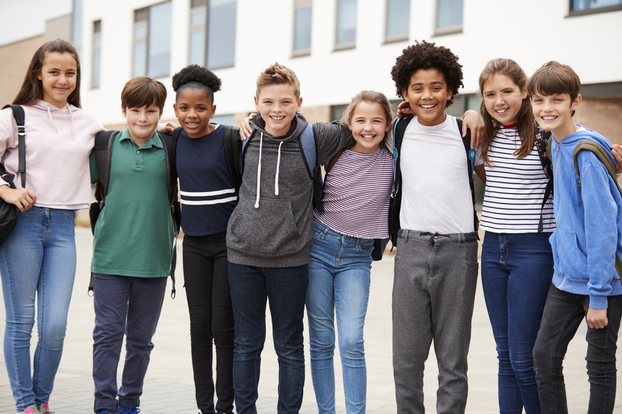 Group of tween kids standing in a line with their arms around each other smiling